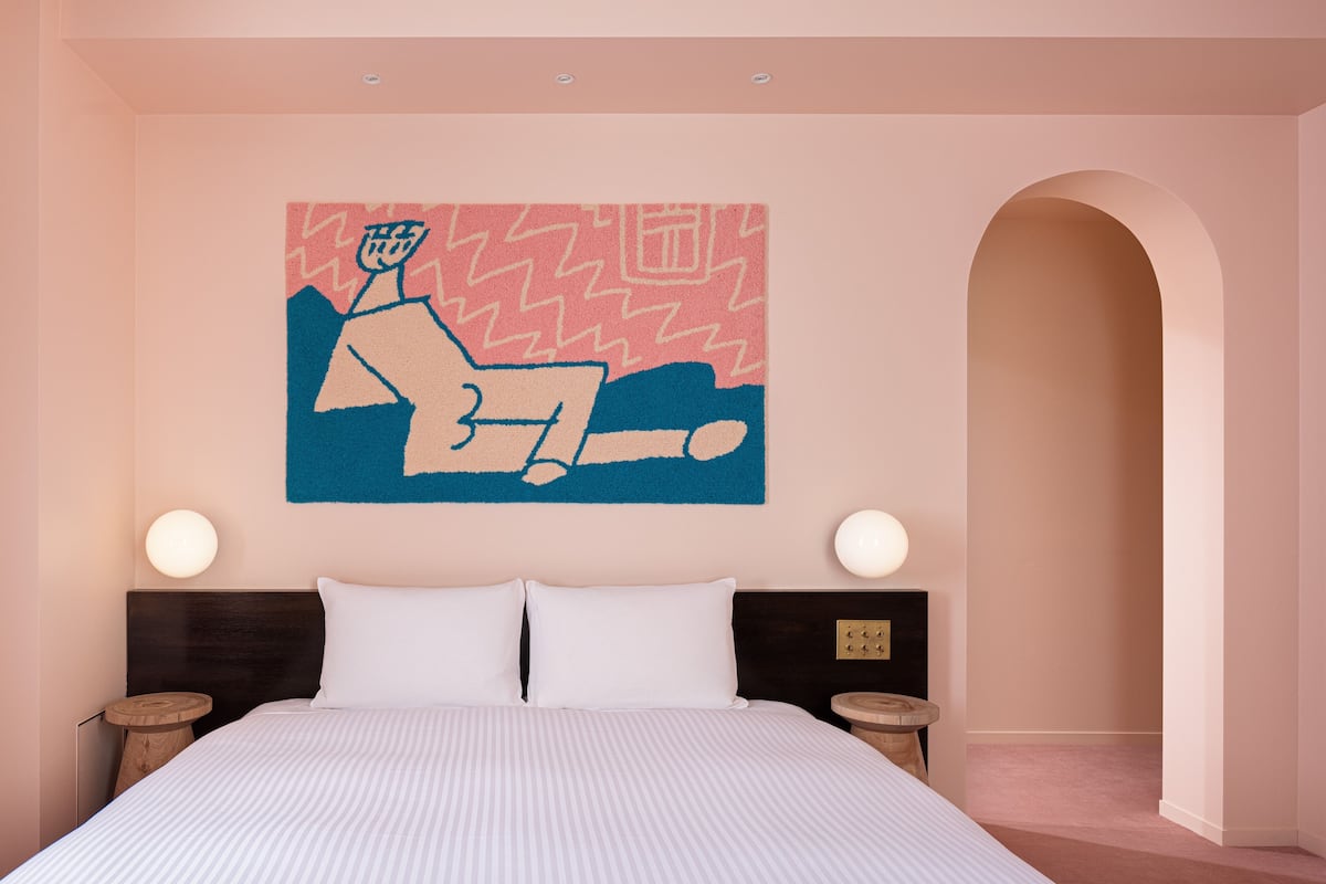 A bedroom with a bed, two bedside tables, a nightstand, and a wall-mounted artwork.