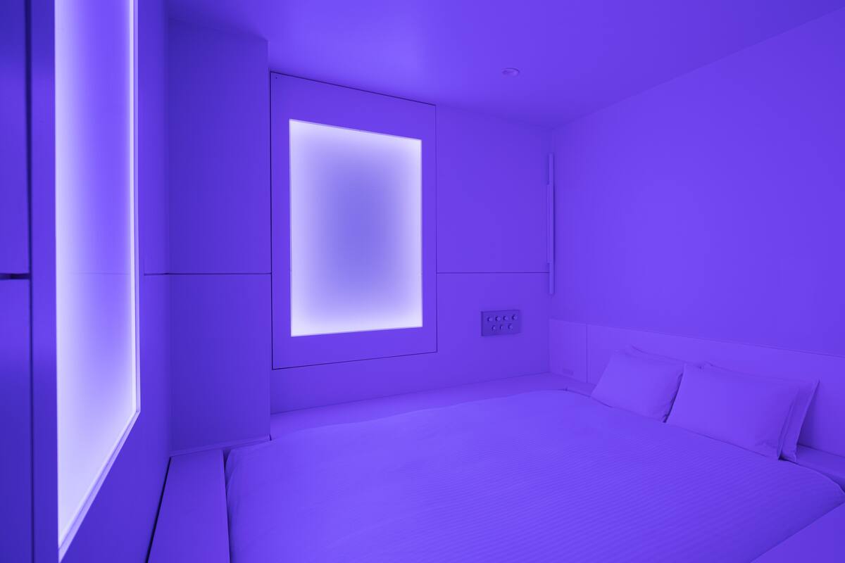 A modern bedroom with a large bed, a wall-mounted TV, and a control panel.