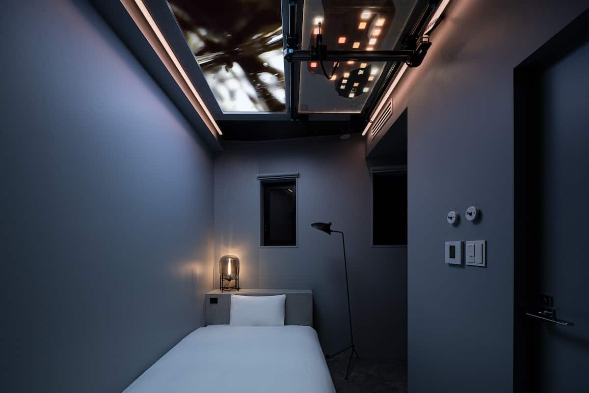 A modern bedroom with a skylight, a bedside lamp, a floor lamp, and a bed.