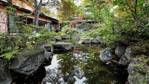 Un jardin japonais traditionnel avec un bassin à carpes koï, des lanternes en pierre et un bâtiment en bois.