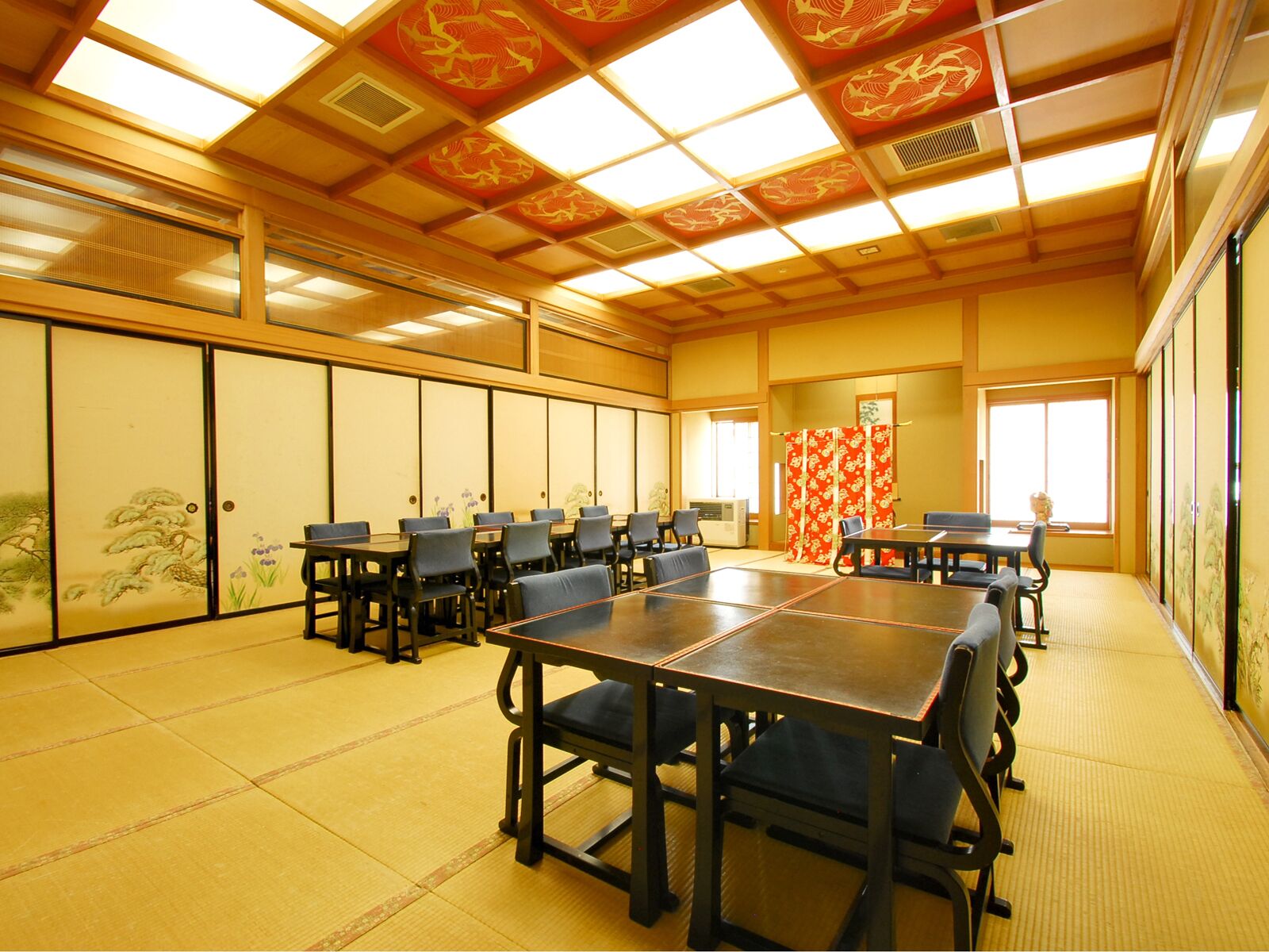 A traditional Japanese meeting room with tatami flooring, low tables, and black chairs.