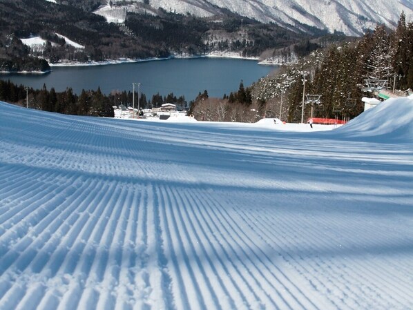 A snow-covered ski slope with a view of a lake and mountains in the background. - Kanouya (Omachi)