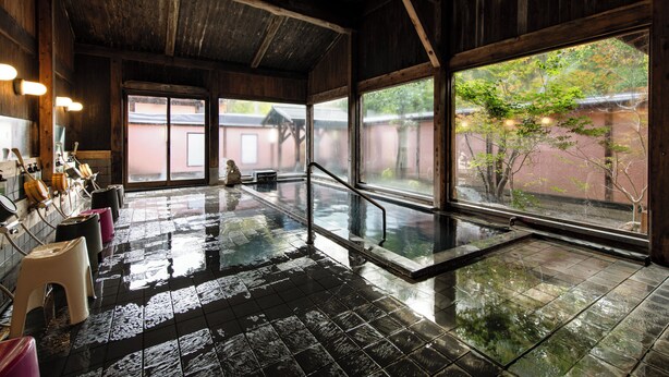 Un onsen japonais traditionnel, avec un intérieur en bois, un sol carrelé et une vue sur l’extérieur.