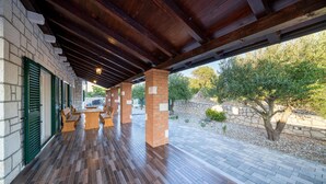 Un porche cubierto con piso de madera, pilares de ladrillo y contraventanas verdes.