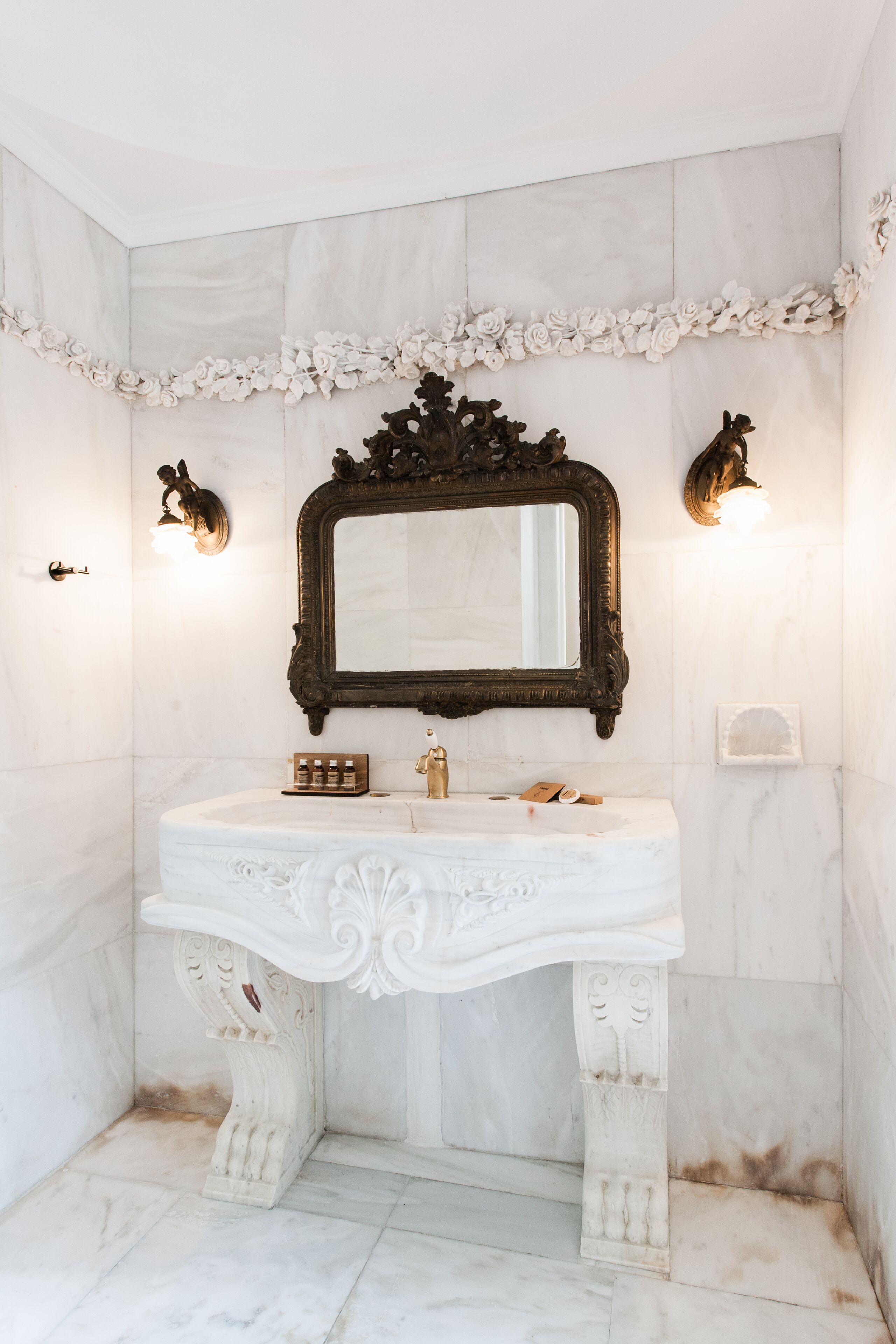 Un bagno con un mobile lavabo in marmo, uno specchio decorato e applique a parete.