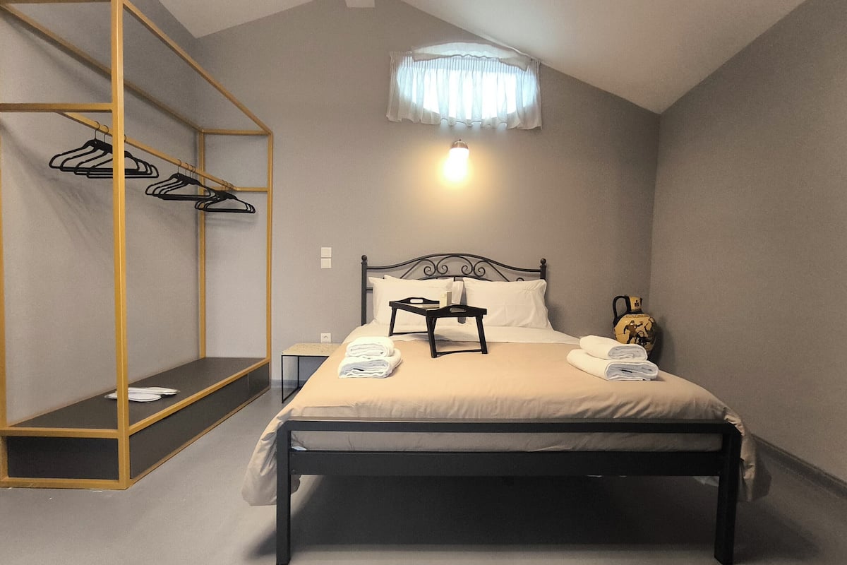 A bedroom with a bed, a bedside table, a hanging coat rack, and a small table with towels.