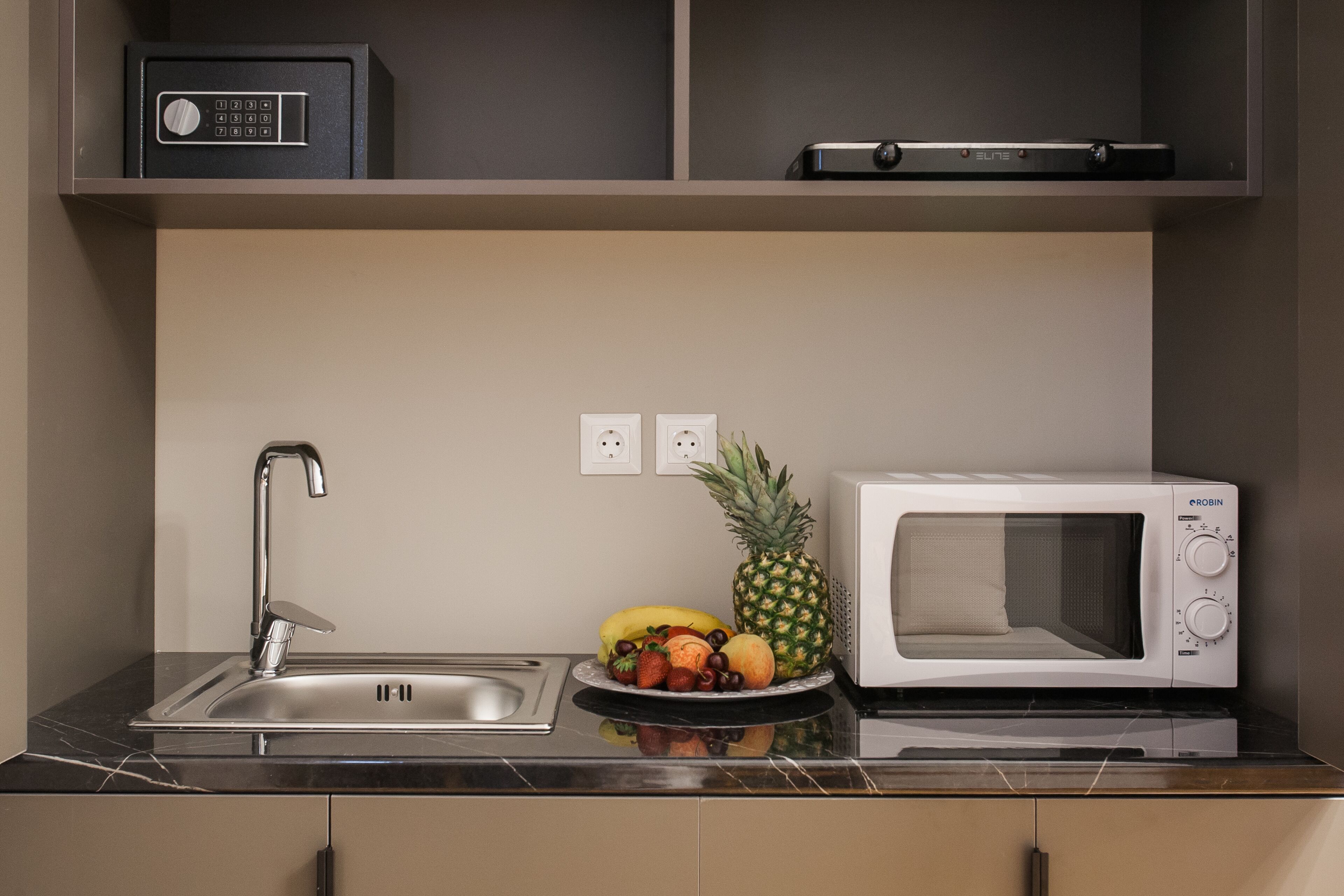 A compact kitchenette with a stainless steel sink, a microwave, and a fruit bowl.