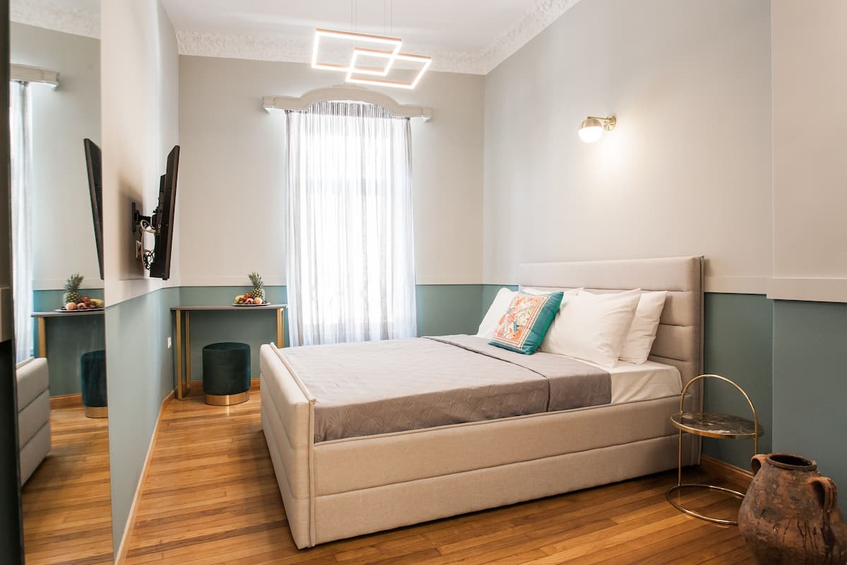A bedroom with a bed, bedside tables, a mirror, a window with curtains, and a vase on the floor.