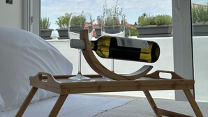 A room with a bed, a wooden wine rack holding a bottle and glasses, and a view of the sky and buildings through a large window. - Step One - Luxury Suites right in the heart of Acropolis next to metro station (Athens)