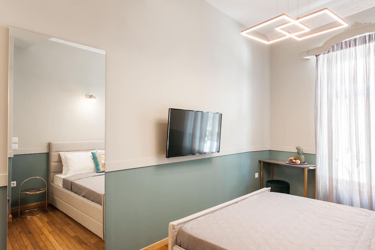 A bedroom with a bed, a TV, a desk, and a window with curtains.