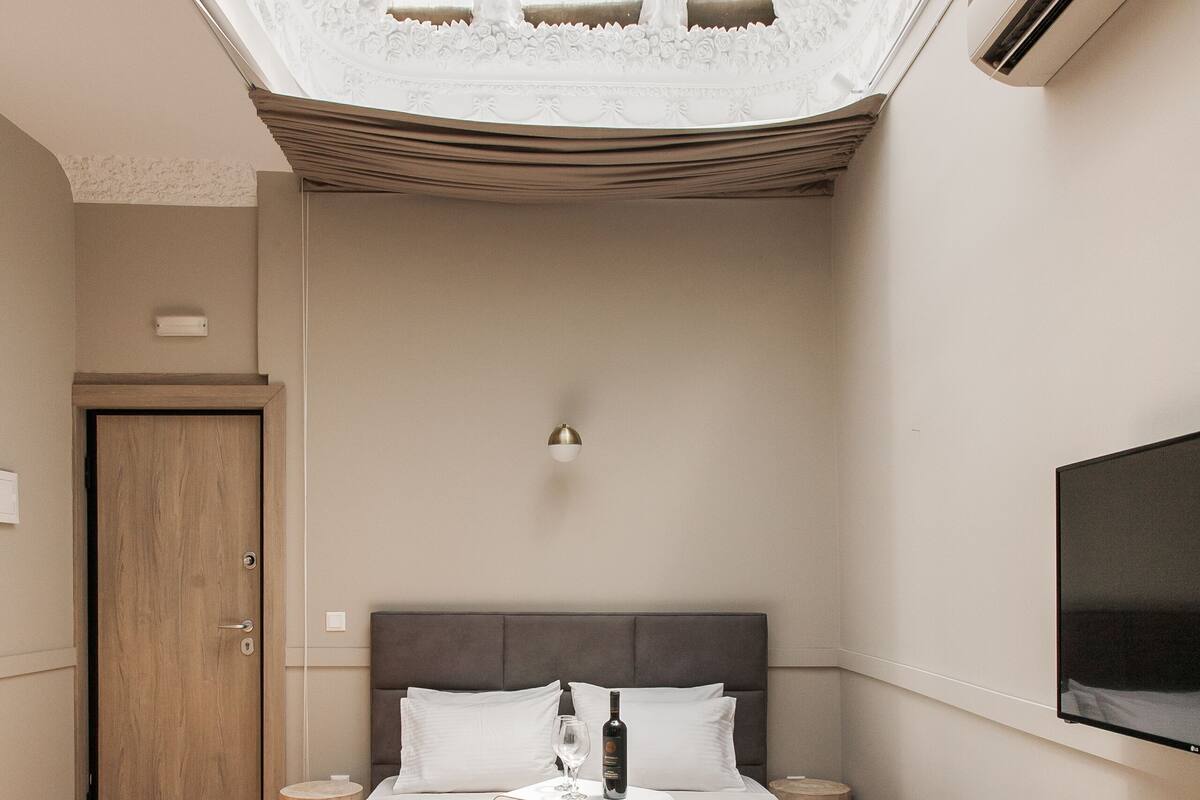 A bedroom with a skylight, a bed, a bench, a bedside table, and a TV.