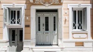A building facade with a central entrance, flanked by two windows with shutters, and a small plaque above the door. - Step One - Luxury Suites right in the heart of Acropolis next to metro station (Athens)