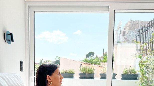 A woman sitting on a bed in a room with a large window, holding a glass of wine. - Step One - Luxury Suites right in the heart of Acropolis next to metro station (Athens)