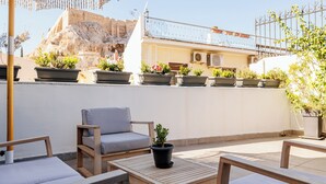 A rooftop terrace with outdoor seating, potted plants, and a view of a historic building. - Step One - Luxury Suites right in the heart of Acropolis next to metro station (Athens)
