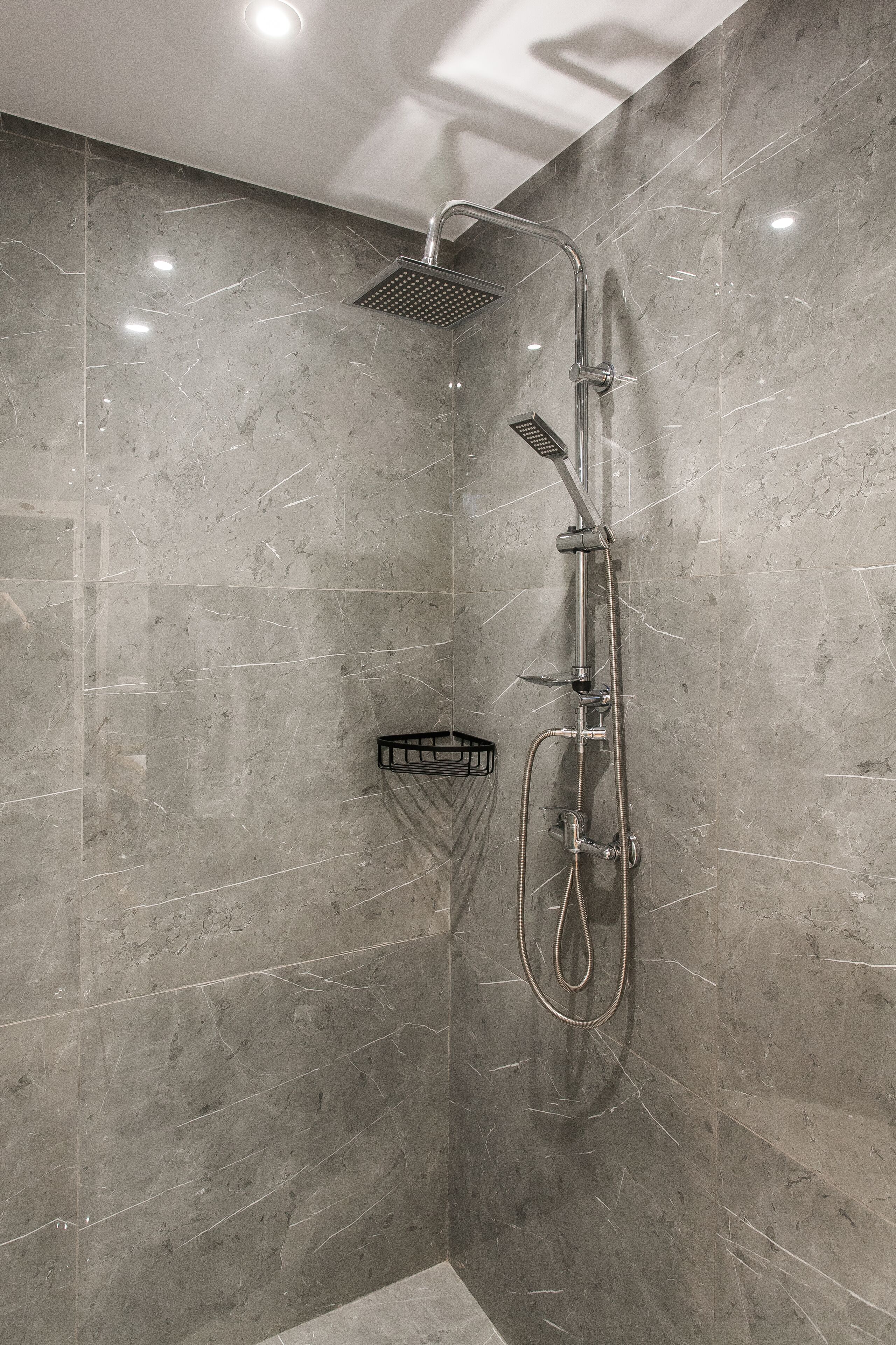 A modern shower with a handheld showerhead, a fixed showerhead, and a handheld shower hose.
