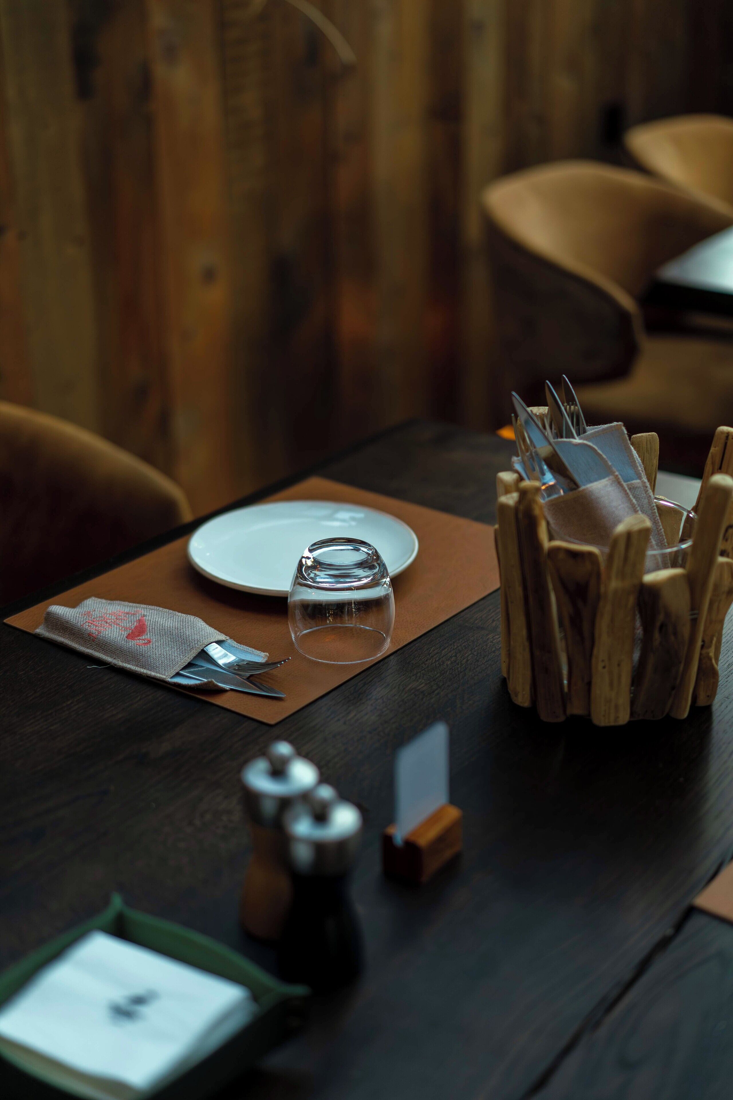 A dining table set with a plate, glass, napkin, and a wooden utensil holder.