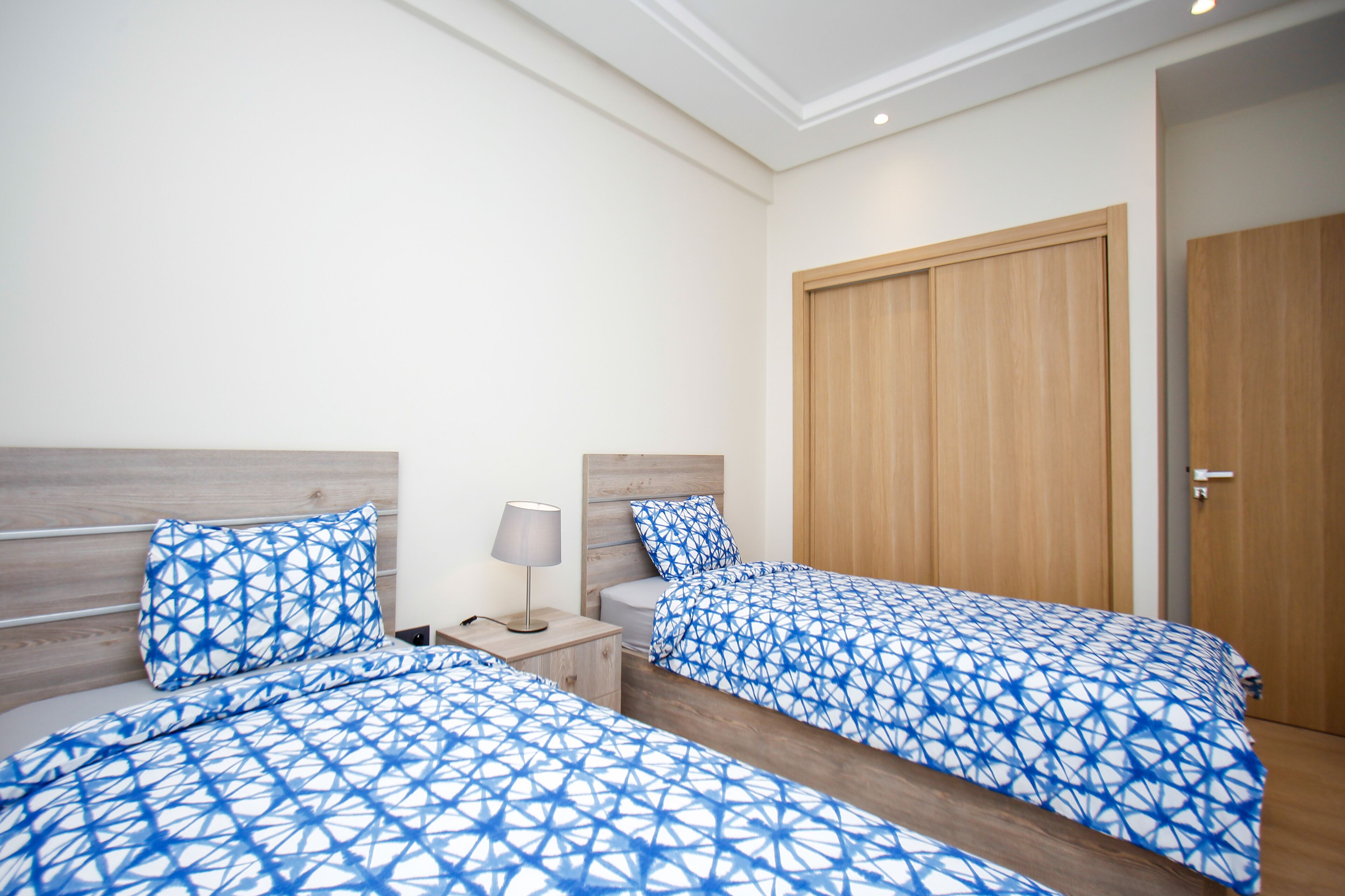 Een hotelkamer met twee bedden, houten hoofdborden, een nachtkastje met een lamp en een houten garderobe.