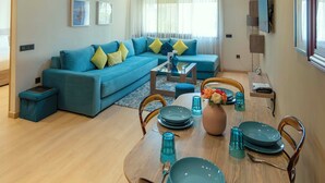 A modern living room with a blue sofa, a dining table set with blue plates, and a television mounted on the wall.