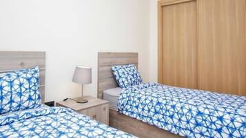 A hotel room with two beds, a nightstand with a lamp, and a wooden wardrobe.