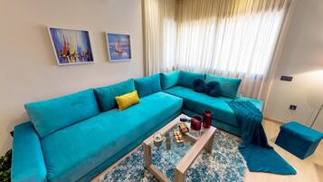 A teal-colored sofa with yellow and dark blue cushions, a coffee table with a teapot and cups, and a blue patterned rug.