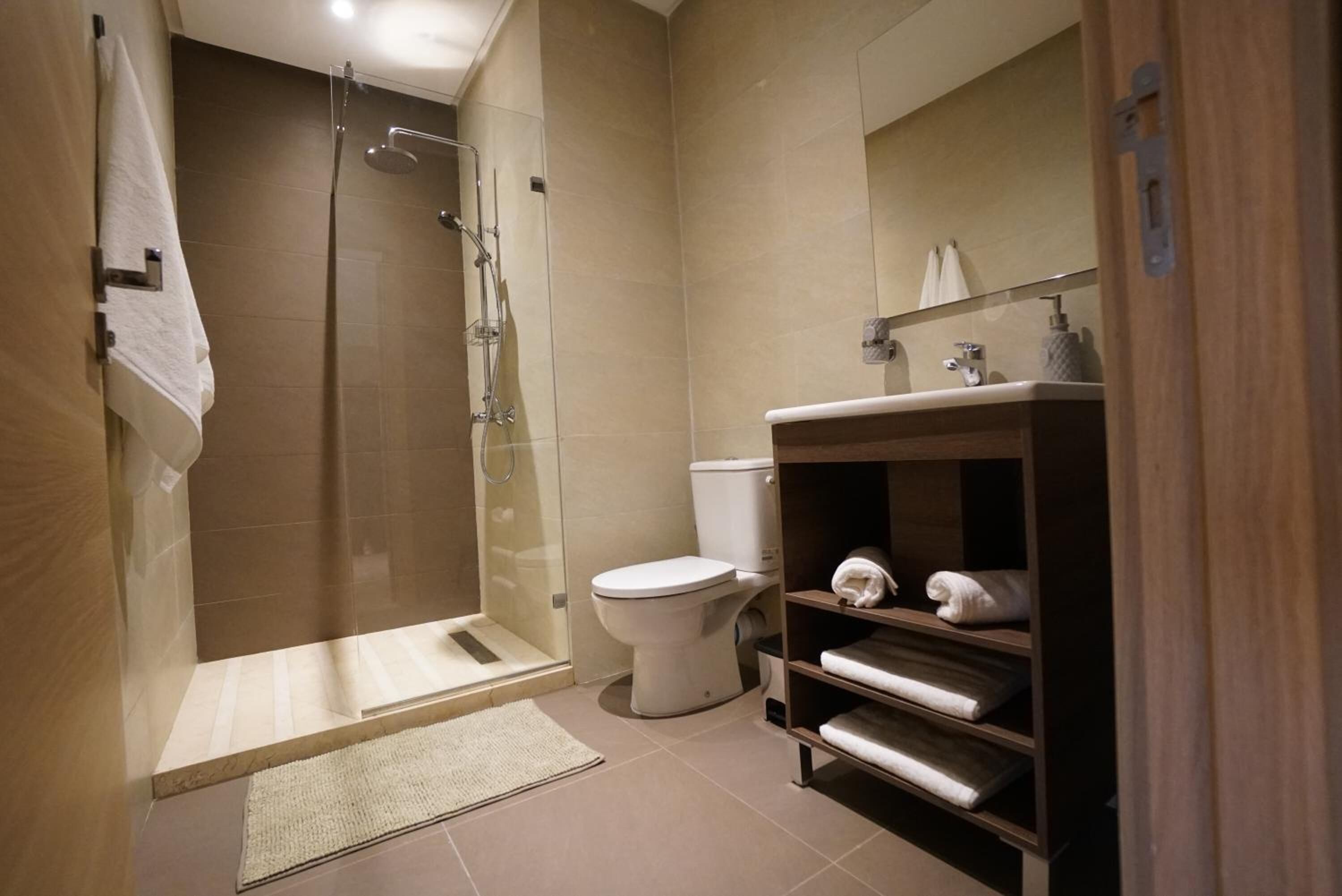 Een moderne badkamer met een douchecabine van glas, een toilet en een houten wastafelmeubel met planken voor handdoeken.