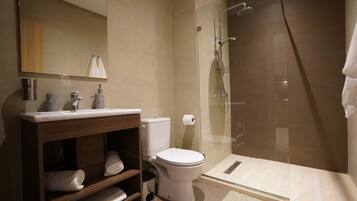 Un baño moderno con inodoro, lavabo y ducha con mampara de vidrio.