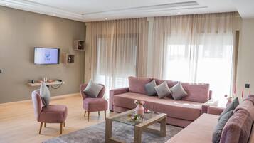 Una sala de estar moderna con un sofá rosa, una mesa de centro de vidrio y un televisor de pantalla plana montado en la pared.