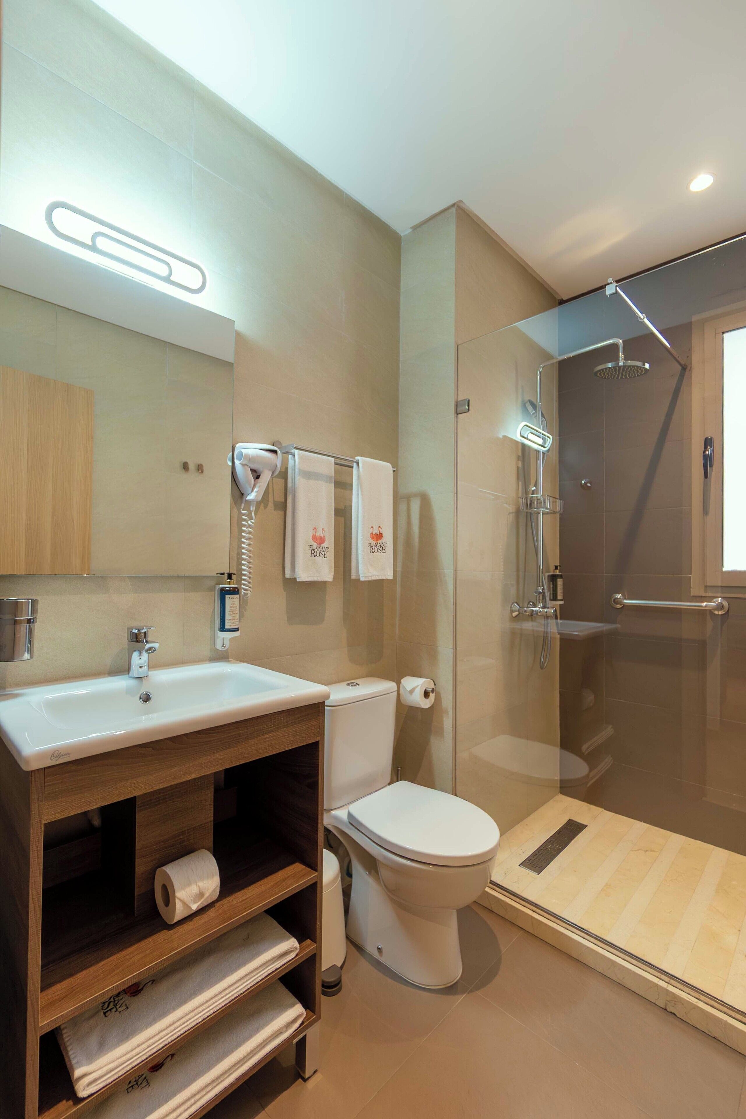 Un baño moderno con ducha envuelta en vidrio, tocador de madera con lavamanos y retrete.
