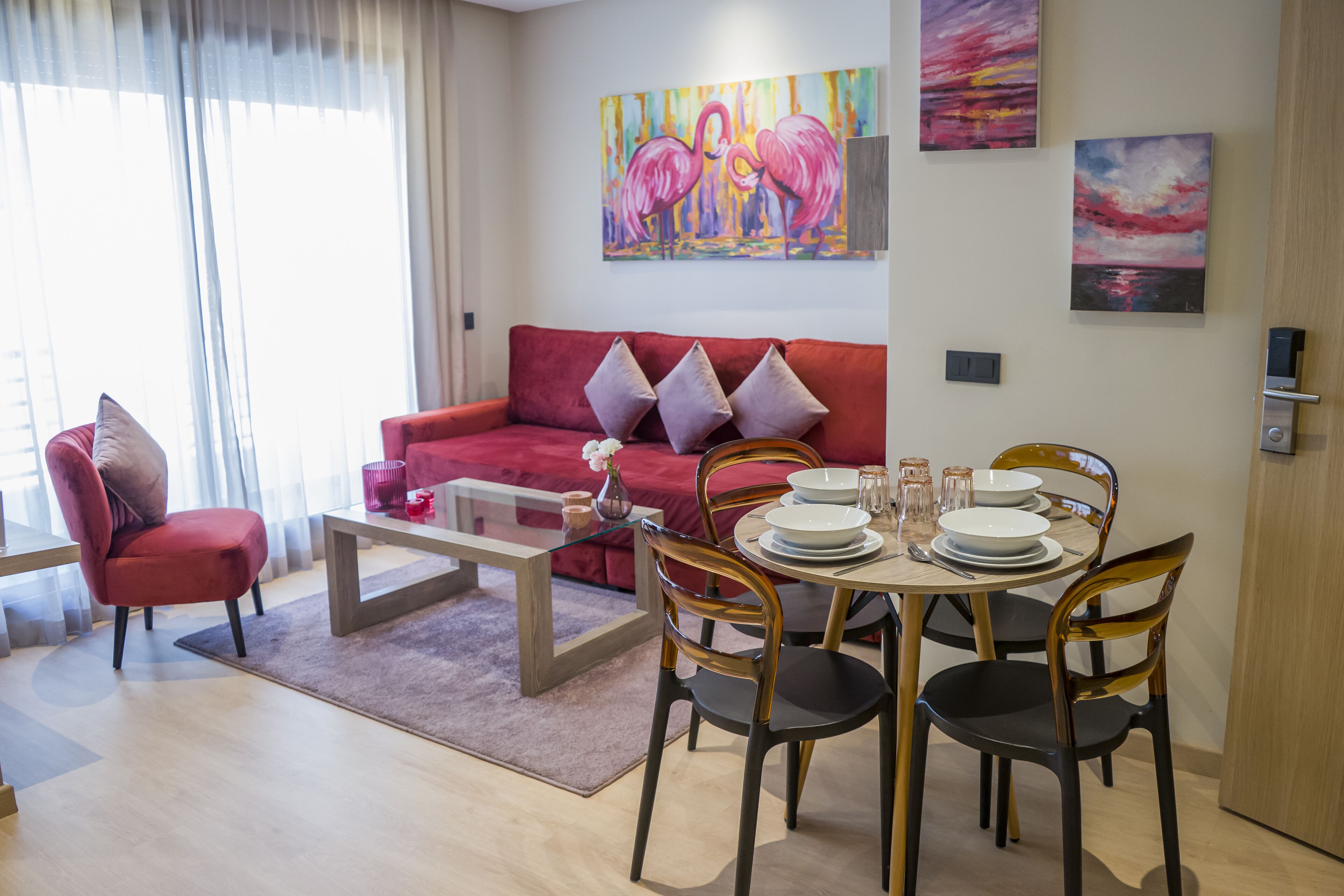 Una sala de estar moderna con un sofá rojo, una mesa de centro de vidrio y un comedor con una mesa y sillas de madera.