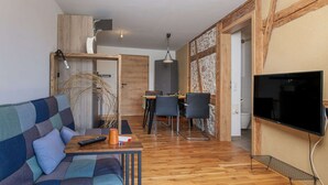 Una sala moderna con sofá, mesa de centro y televisor. Hay una zona de comedor con mesa y sillas. El piso es de madera y una pared de acento de piedra.
