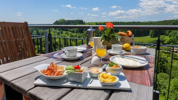 Una mesa preparada para el desayuno, con diversos platos y bebidas, con vistas a un paisaje pintoresco.