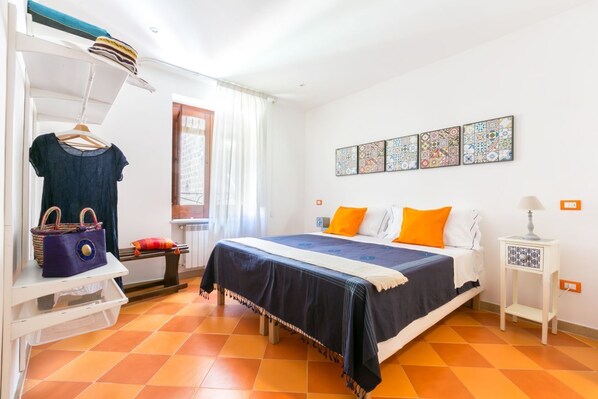 A bedroom with a bed, a dresser, a hanging rack, a window, and a wall with artwork.