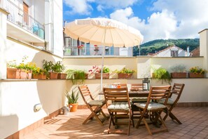 A patio with a table and chairs, surrounded by potted plants and an umbrella.