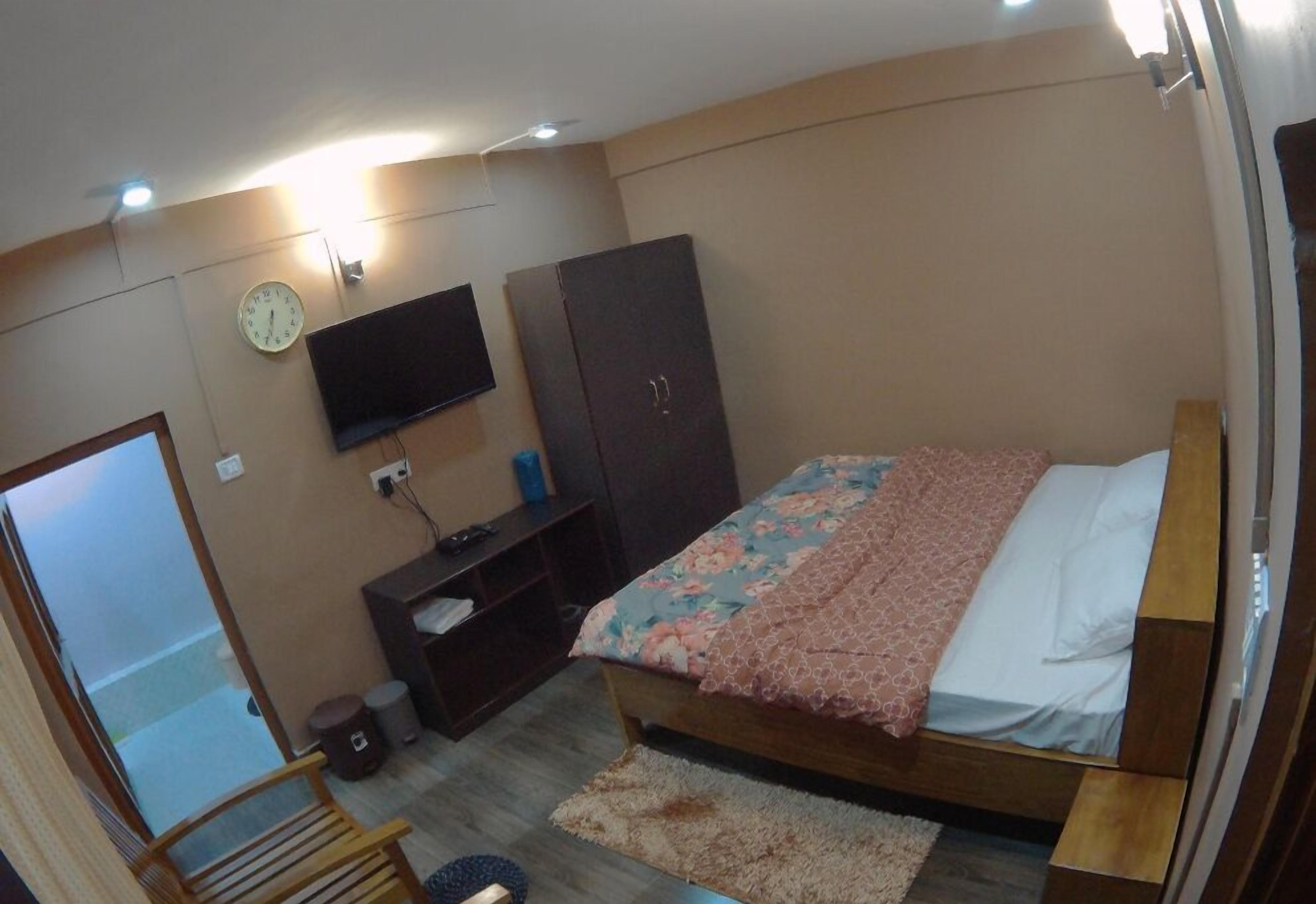 A bedroom with a bed, a wardrobe, a television, and a clock on the wall.