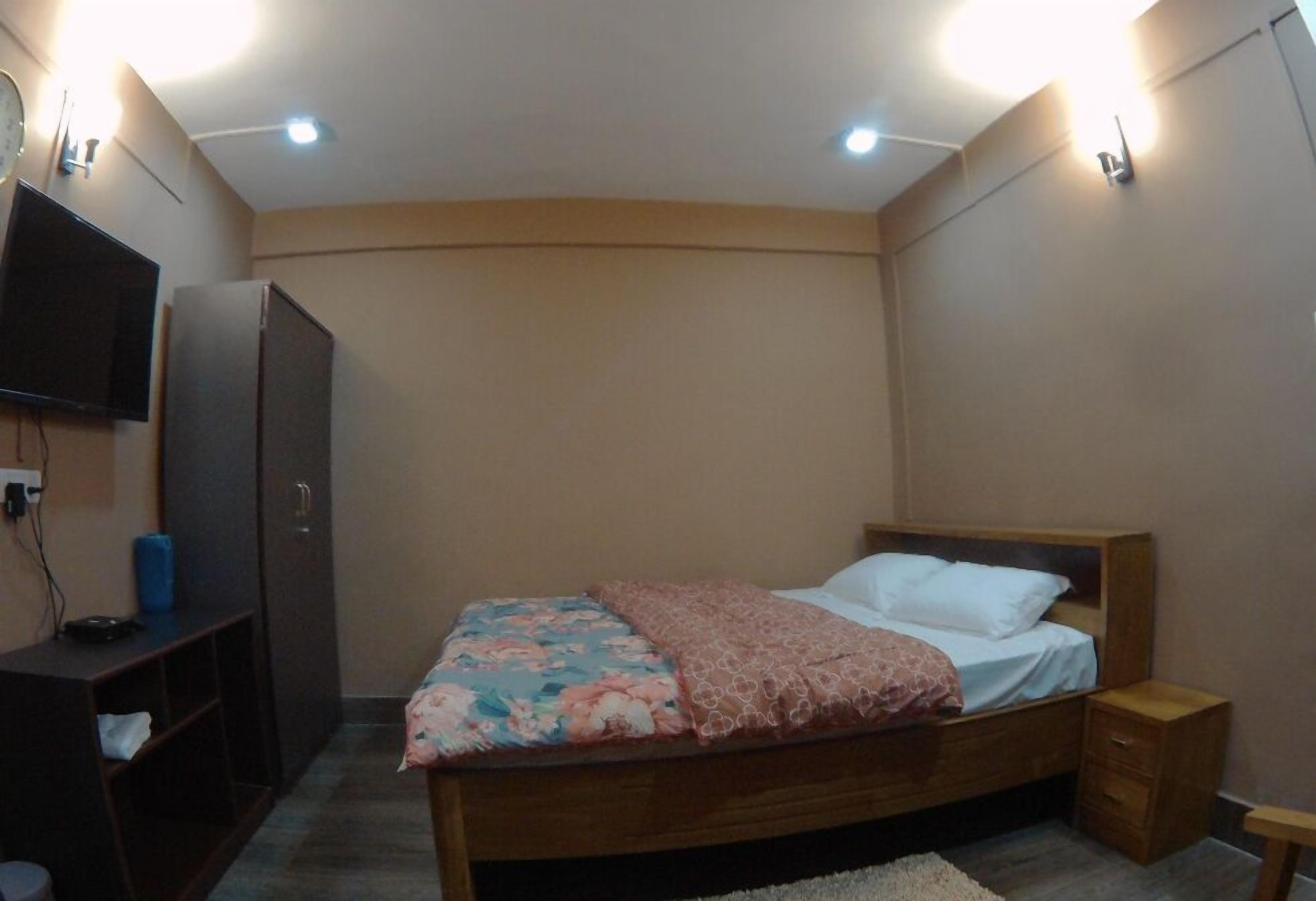 A bedroom with a bed, a TV mounted on the wall, and a wardrobe.