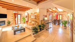 A spacious living area with a stone fireplace, a sofa, a coffee table, and a dining area with a bar. - Cretan Dream Villa (Apokoronas)