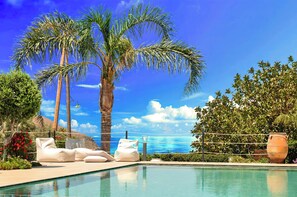 A poolside area with lounge chairs, a palm tree, and a view of the ocean. - Cretan Dream Villa (Apokoronas)