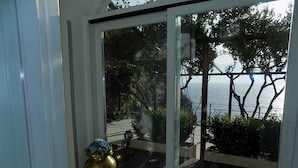Ein Zimmer mit einer großen Schiebetür zu einem Balkon mit Blick auf das Meer und Bäume.