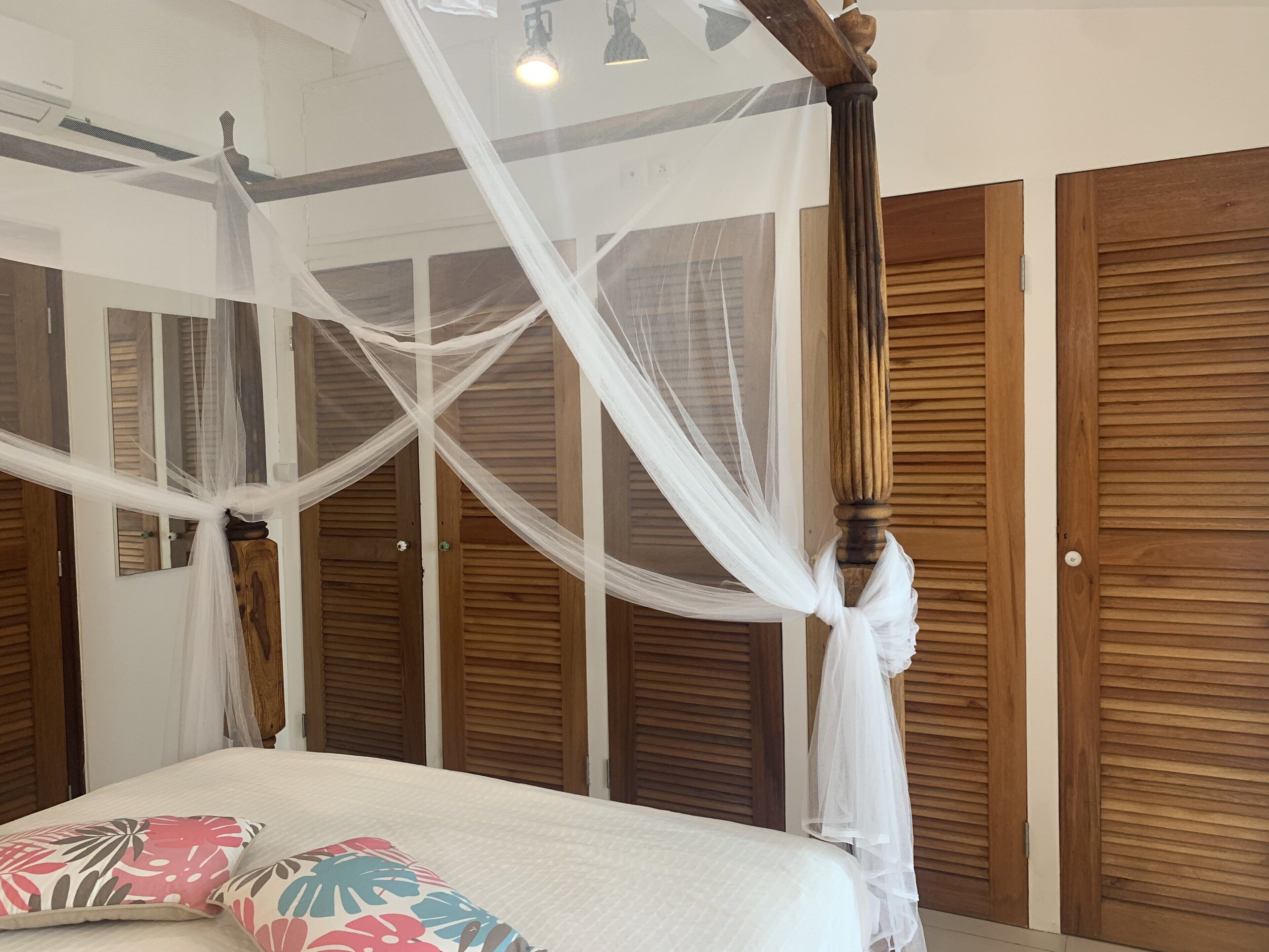 A bedroom with a four-poster bed, wooden paneling on the walls, and a ceiling fan.