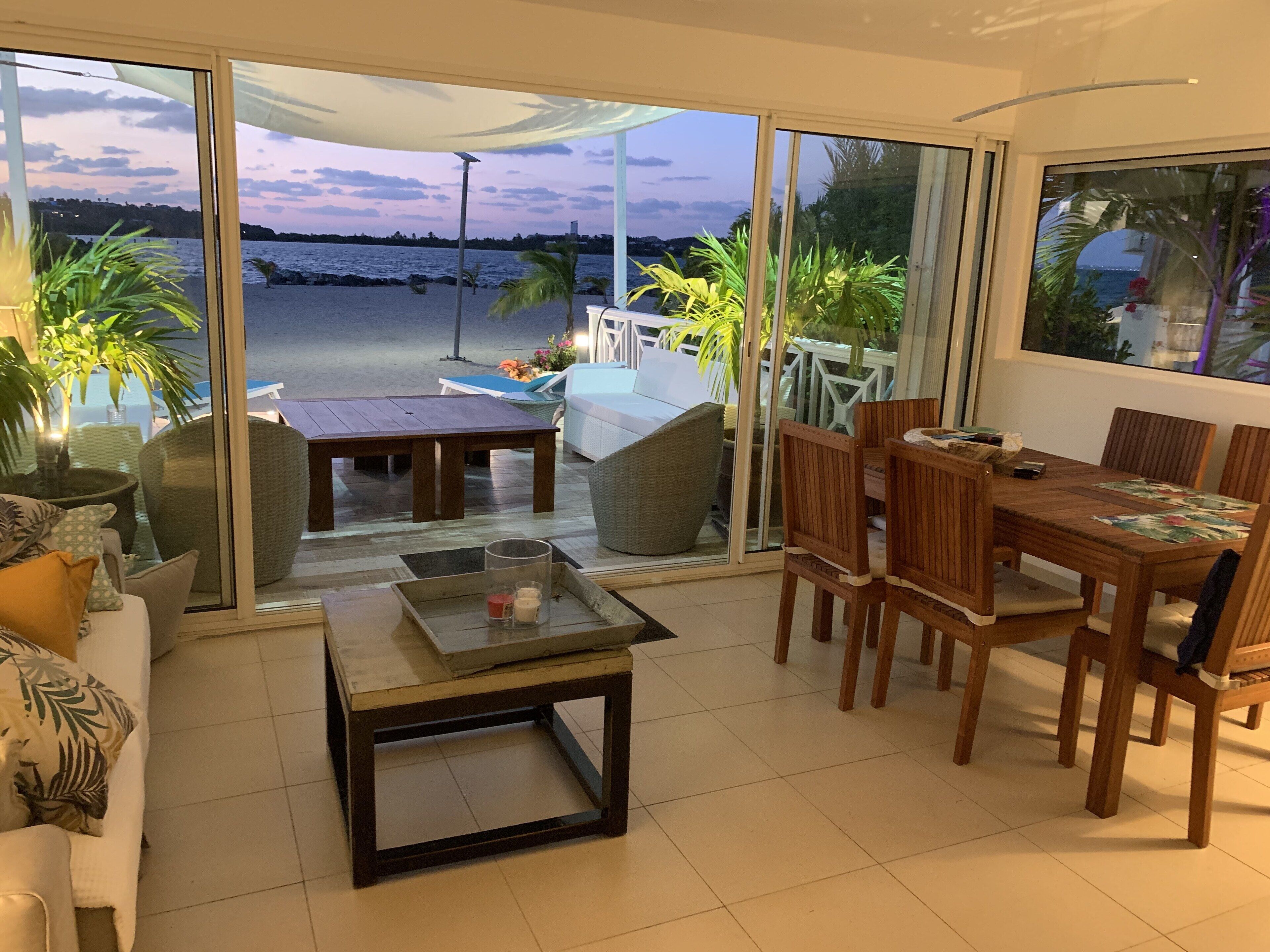 A spacious living area with a large sliding glass door leading to a balcony overlooking a beach.