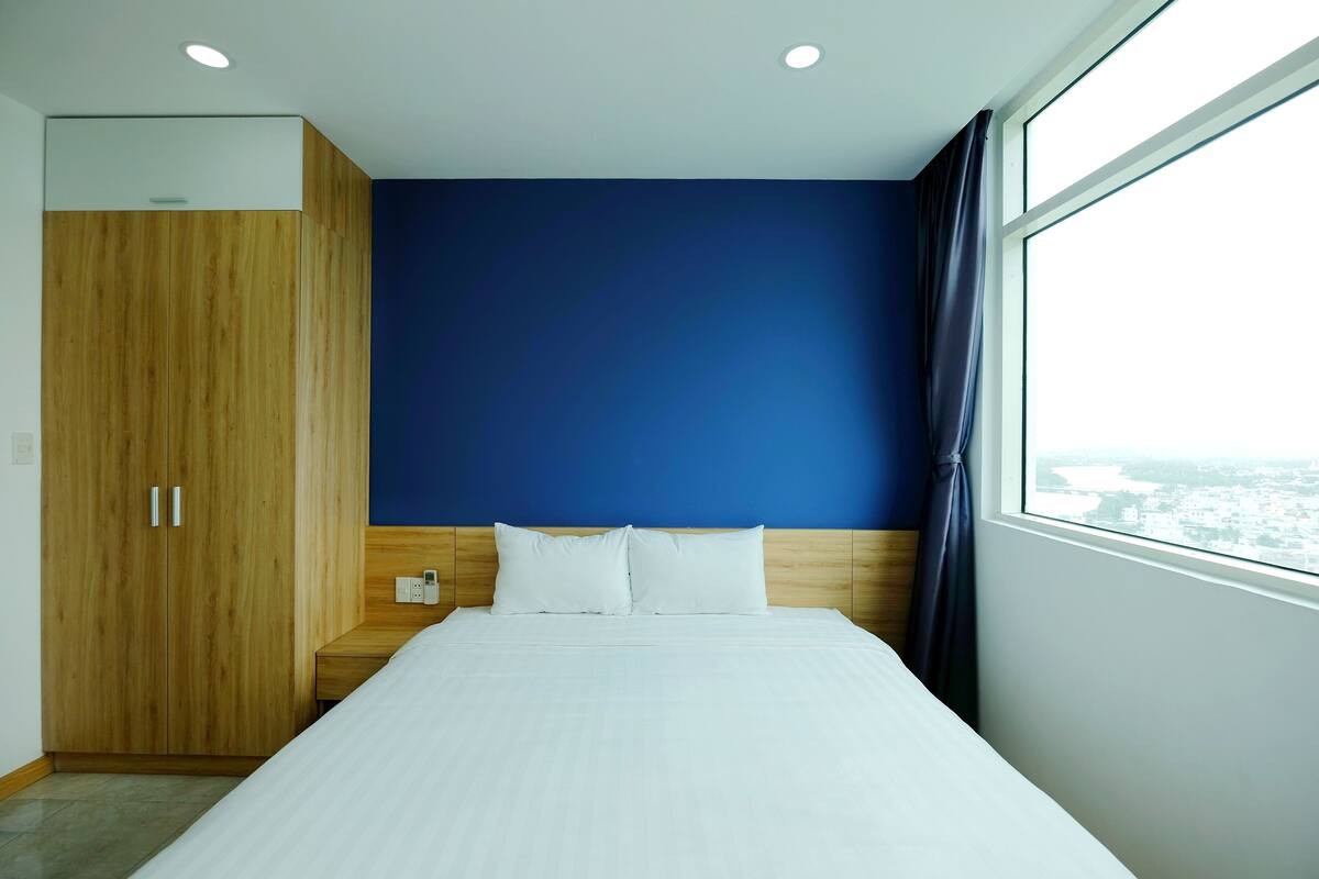 A hotel room with a bed, wooden wardrobe, and a window with a city view.