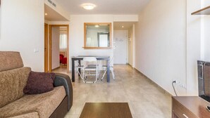 A modern living room with a sofa, a dining table with chairs, a TV, and a small wooden cabinet. - DON PEDRO APARTMENT IN ALCOCEBRE (Alcocéber)