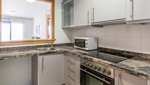 A compact kitchen with white cabinets, a microwave, a stove, and a sink. - DON PEDRO APARTMENT IN ALCOCEBRE (Alcocéber)