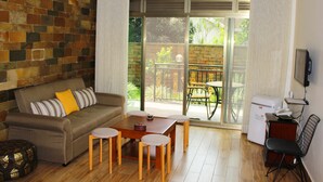 Ein Wohnzimmer mit einer Couch, einem Tisch und Stühlen, einem Kühlschrank und einer Glasschiebetür, die zu einem Außenbereich mit Tisch und Stühlen führt.
