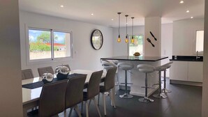 Een moderne keuken met een eethoek, met een groot schiereiland met barkrukken, een eettafel met stoelen en een wandklok.