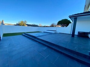 Um terraço no telhado com hidromassagem, uma pequena área gramada e uma parede branca.