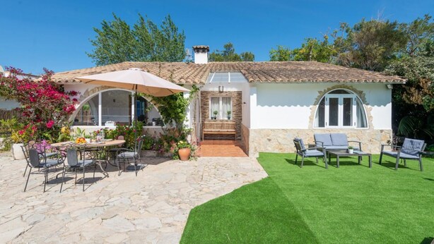 A house with a stone patio, a small garden, and outdoor seating.