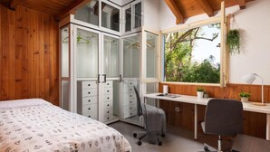 A bedroom with a bed, a desk, and a wardrobe with glass doors.
