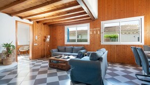 A spacious living room with a checkered floor, wooden walls, and a large window with a view of a house.