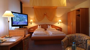 A hotel room with a bed, a television, a desk with a lamp, and a wardrobe. - Hotel Anika (Neuenburg am Rhein)